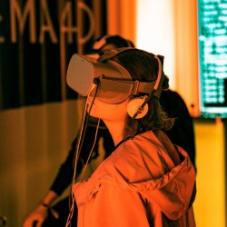 Kuvassa on oranssitakkinen henkilö, jolla on VR-lasit päässään.